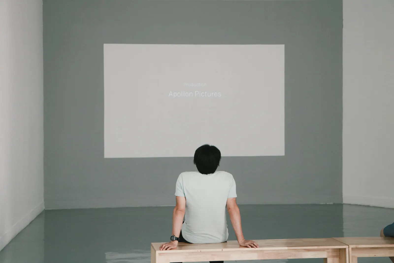 Person seated on a bench watching a projected presentation on a white wall
