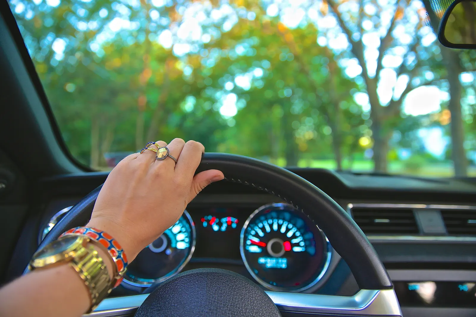 Hand resting on a car steering wheel with the dashboard gauges visible