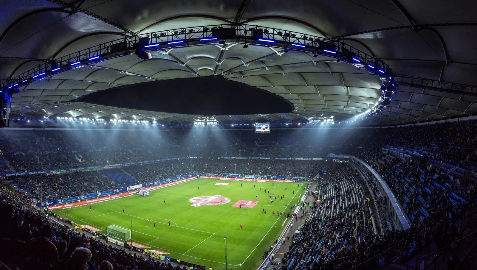 Packed soccer stadium at night under bright floodlights with fans in the stands