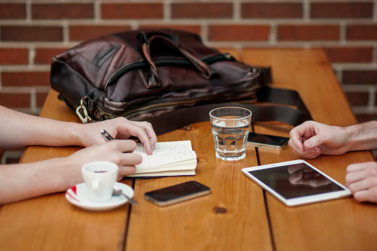 Two people meeting at a wooden table with a notebook, tablet, phone and coffee