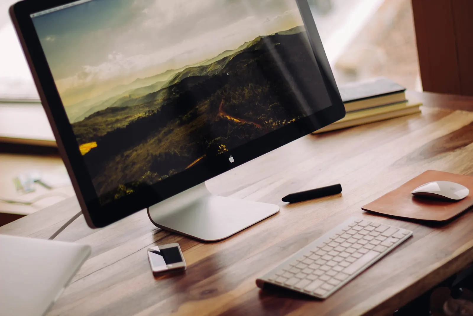 Clean computer desk setup with a large monitor, keyboard and mouse on a wooden desk