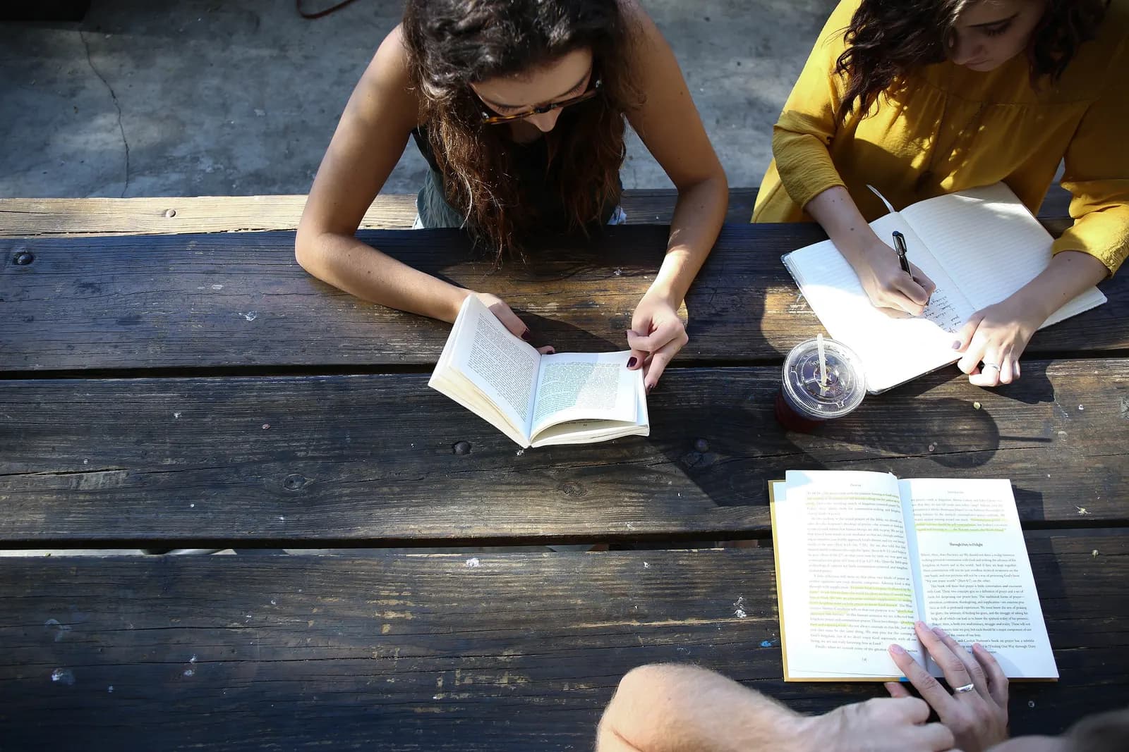 Two students studying together at a wooden table with open books and notebooks